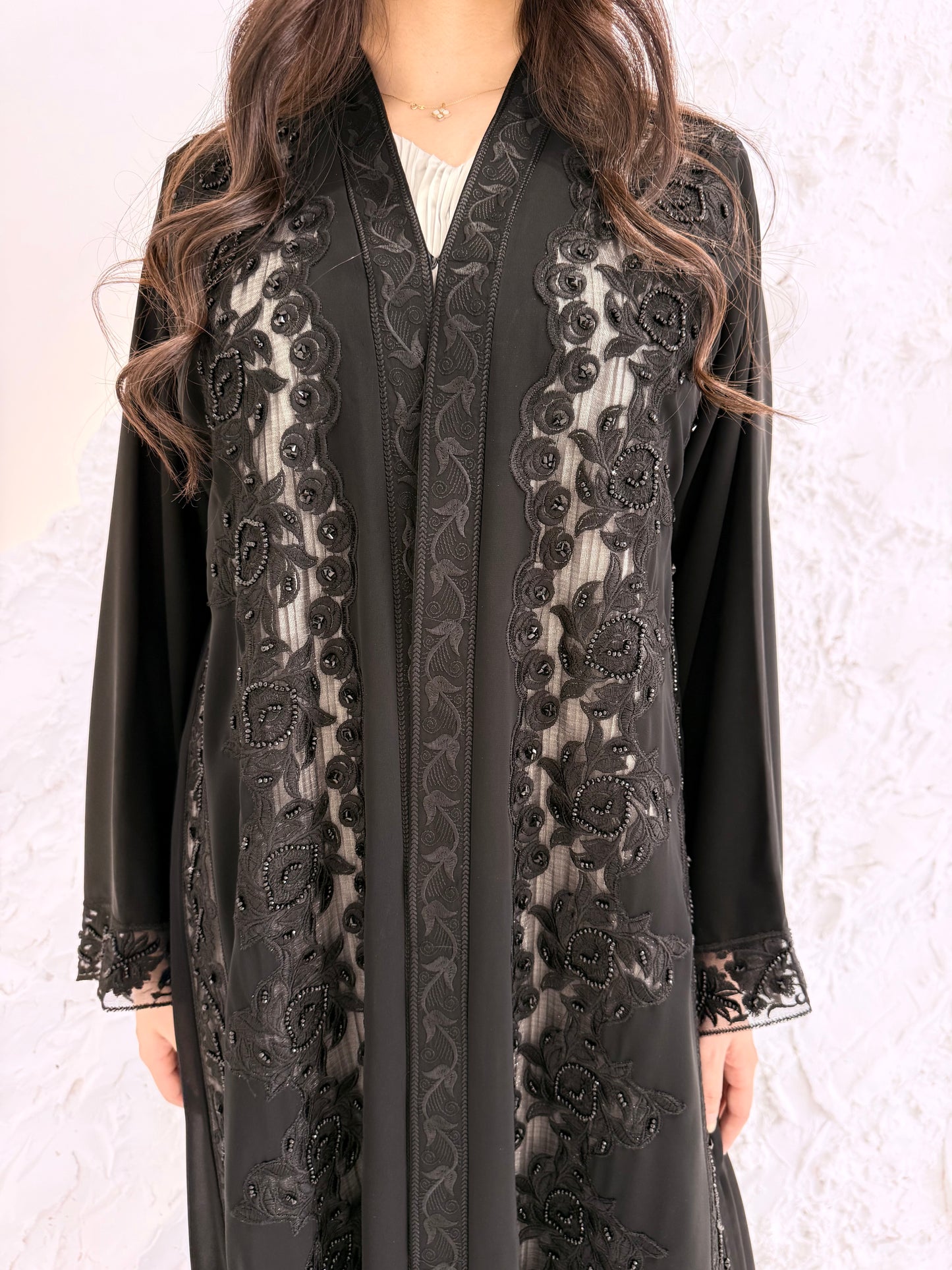 Woman wearing a Premium Black Hand-Embellished Abaya against a white textured wall