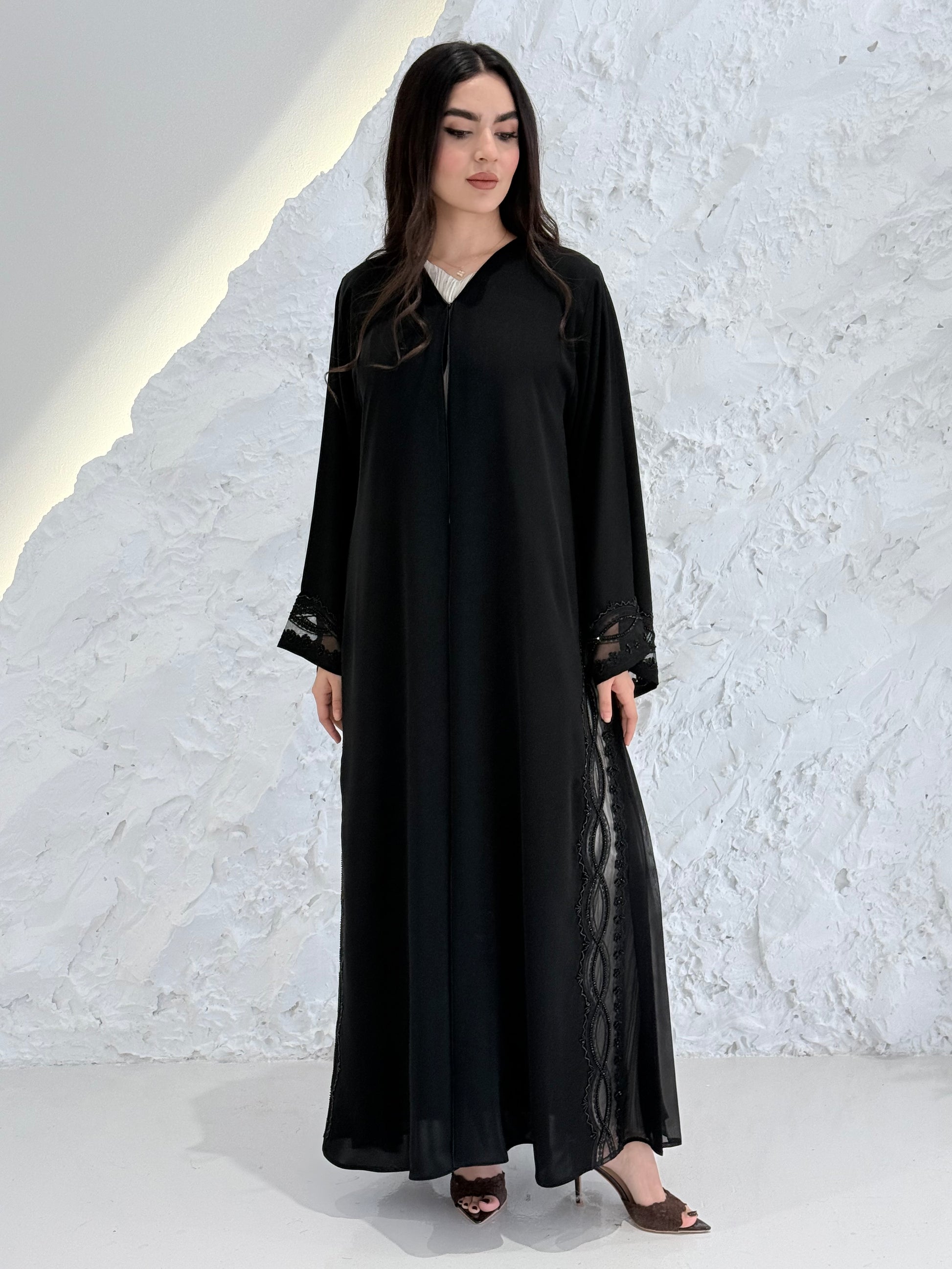 Woman wearing a  Premium Black Abaya with Black Plissé Panel on a light gray background