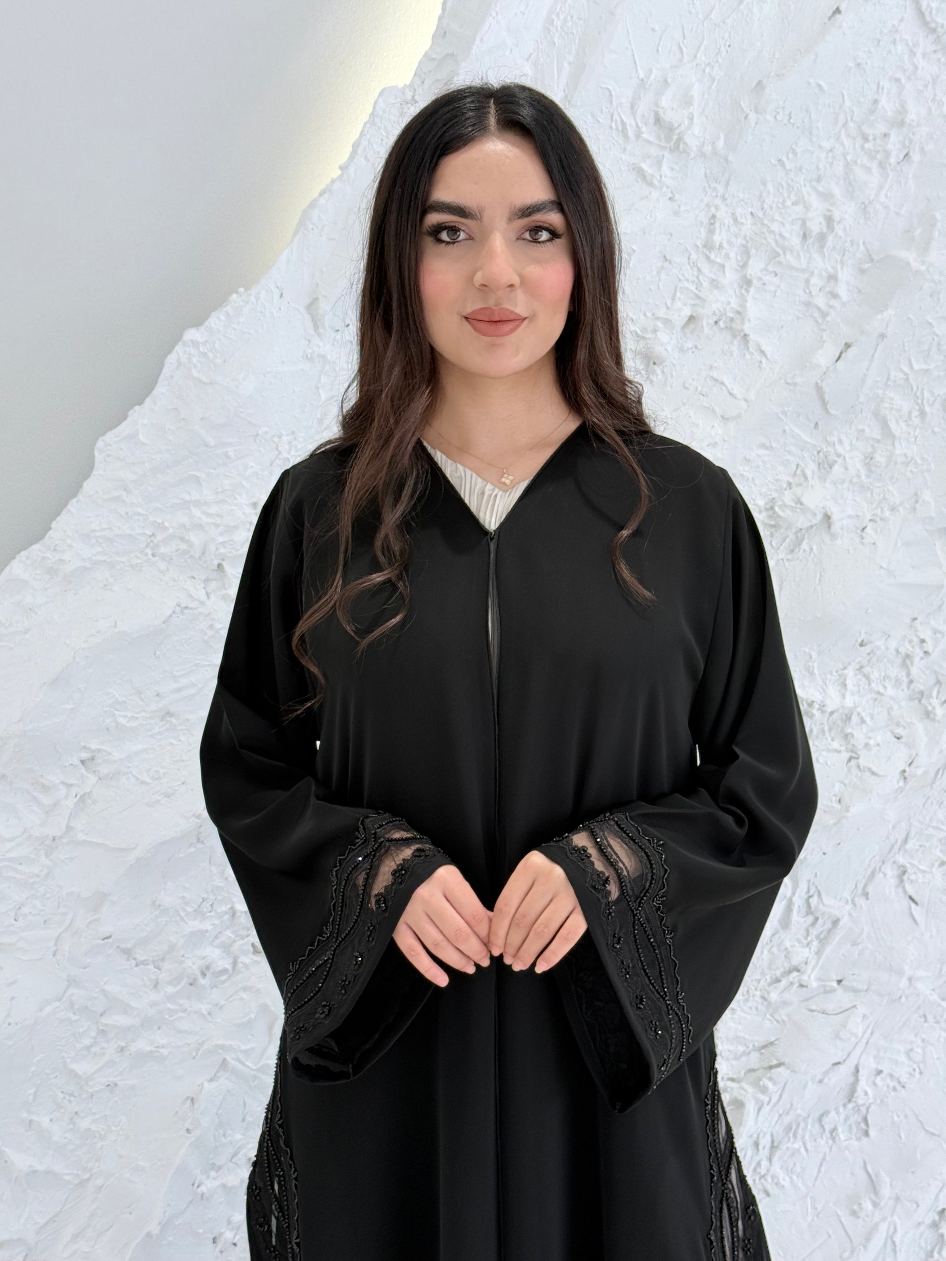 Woman wearing a  Premium Black Abaya with Black Plissé Panel on a light gray background