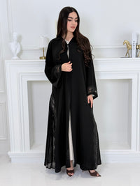 Woman wearing a  Premium Black Abaya with Black Plissé Panel on a light gray background