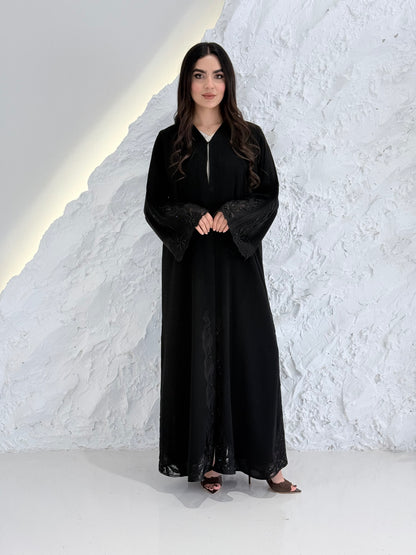 Woman wearing a  Premium Black Abaya with Black Plissé Panel on a light gray background