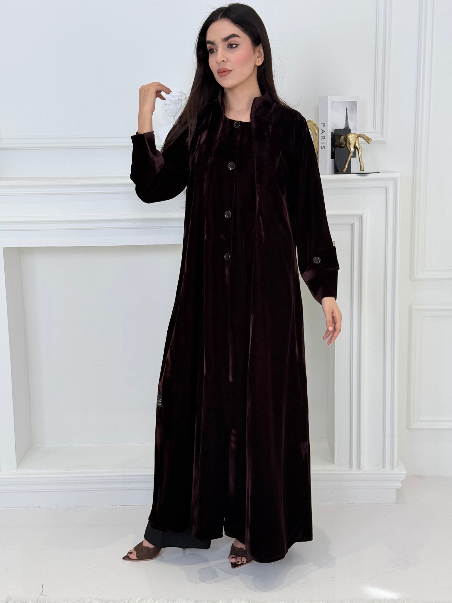 Woman wearing a long Dark Chocolate Velvet Trench Abaya coat in a minimal white room