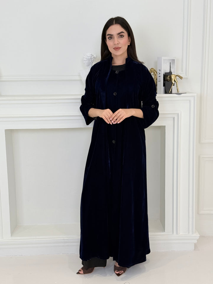 Woman in a Navy Blue Velvet Trench Abaya outfit standing in front of a white door.