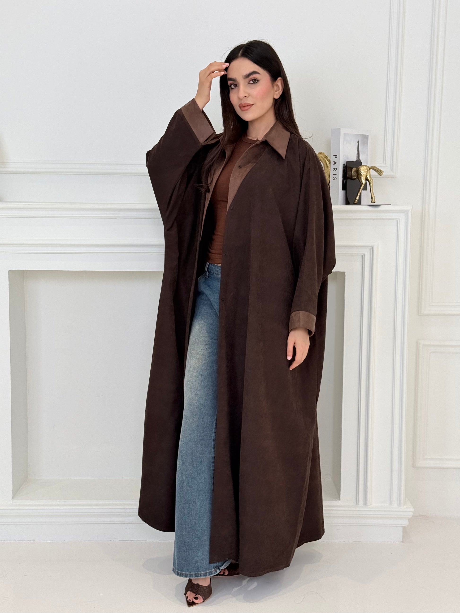Woman wearing a long brown coat in a minimalistic room.