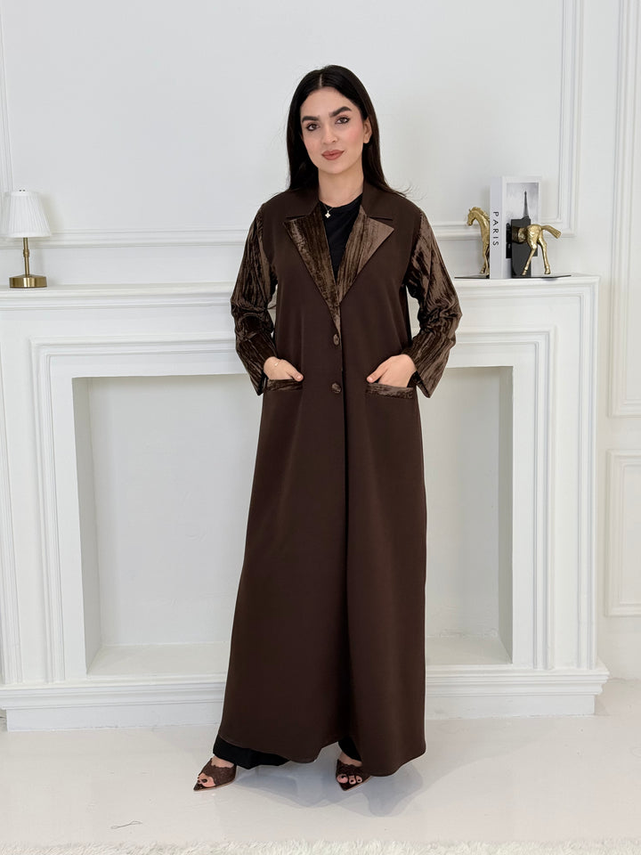 Woman wearing a long dark brown coat-style abaya made from Premium Barbie (Body) and Crushed Velvet in a white interior setting