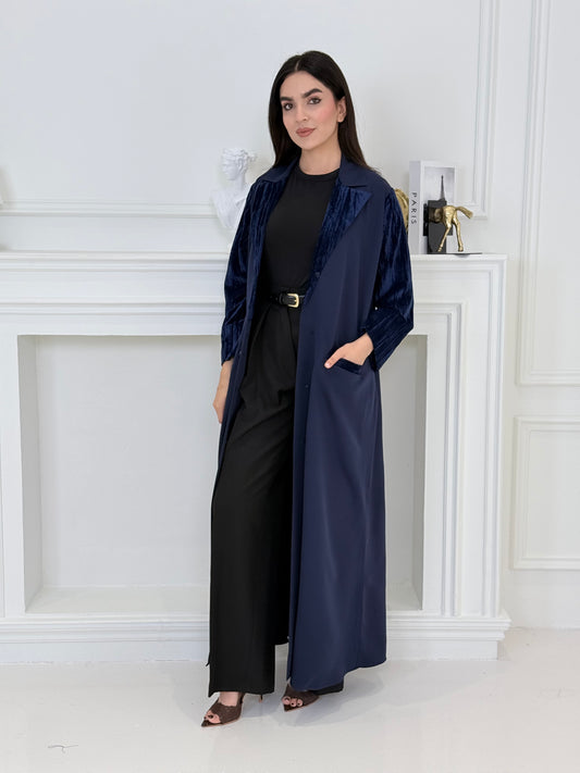Woman wearing a long navy blue coat-style abaya made from Premium Barbie (Body) and Crushed Velvet in a white interior setting
