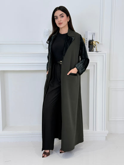 Woman wearing a long olive green coat-style abaya made from Premium Barbie (Body) and Crushed Velvet in a white interior setting