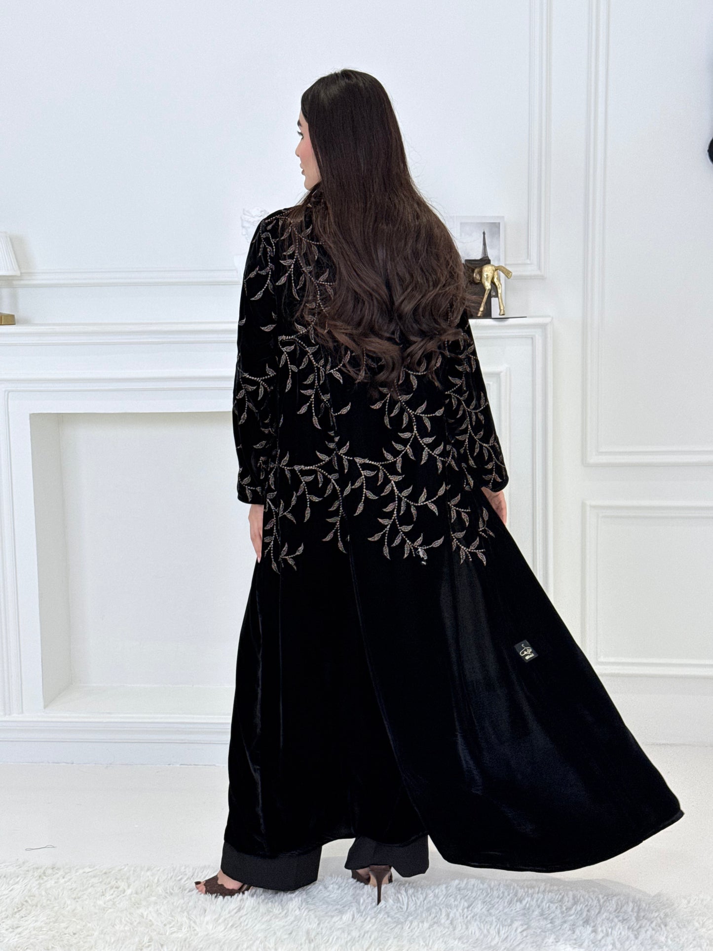 Person wearing a Premium Velvet Abaya with Gold Vine floral Embroidery patterns in a room with white walls.