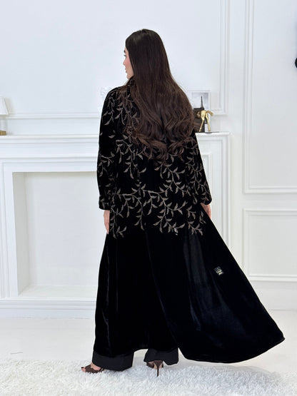 Person wearing a Premium Velvet Abaya with Gold Vine floral Embroidery patterns in a room with white walls.