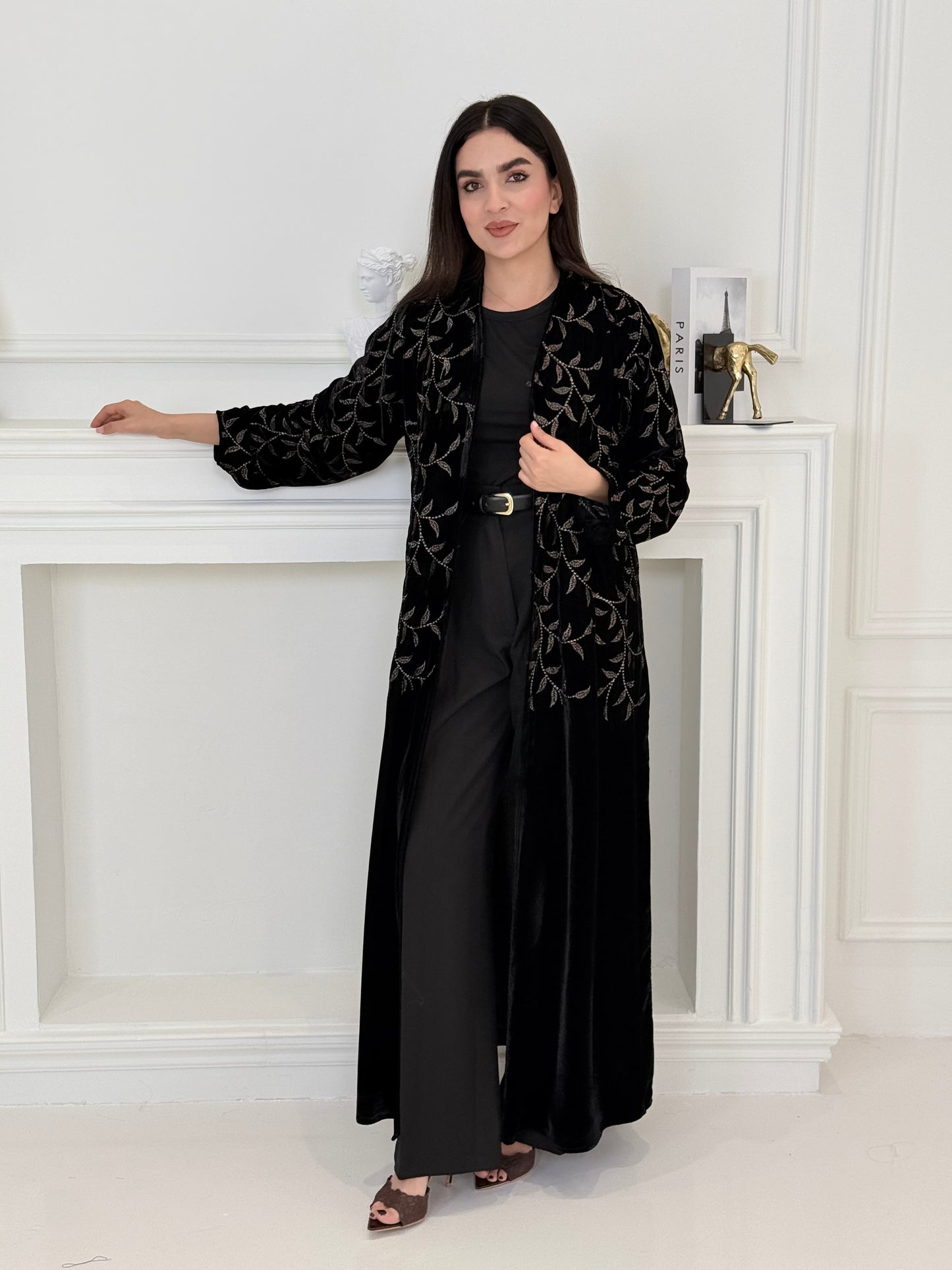 Person wearing a Premium Velvet Abaya with Gold Vine floral Embroidery patterns in a room with white walls.