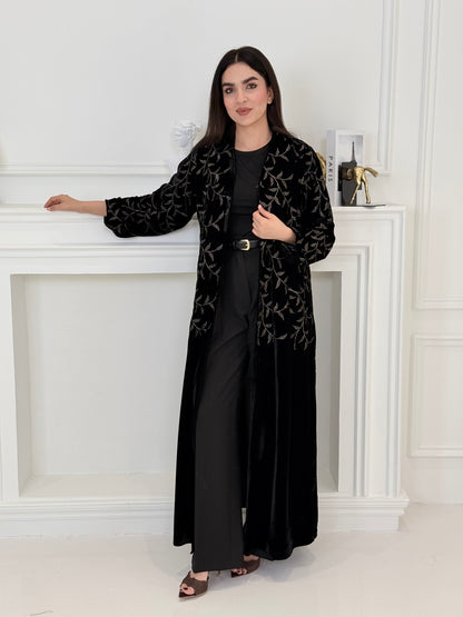 Person wearing a Premium Velvet Abaya with Gold Vine floral Embroidery patterns in a room with white walls.