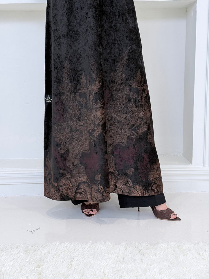 A woman wearing a in Black Velvet Abaya with Bronze & Maroon Details a white room