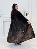 A woman wearing a in Black Velvet Abaya with brown & green Details a white room