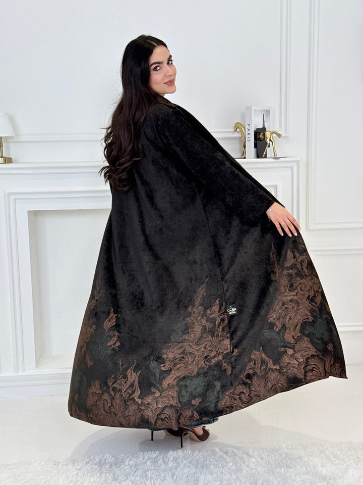 A woman wearing a in Black Velvet Abaya with brown & green Details a white room