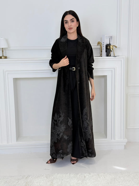Woman wearing a Black Velvet Abaya with Silver & Grey Details with floral patterns in a minimalistic room.