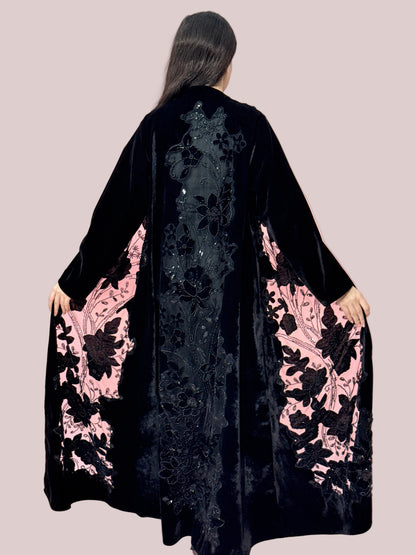 woman wearing a Premium Black Velvet Abaya with Floral Embroidery, lace garment on a pink background