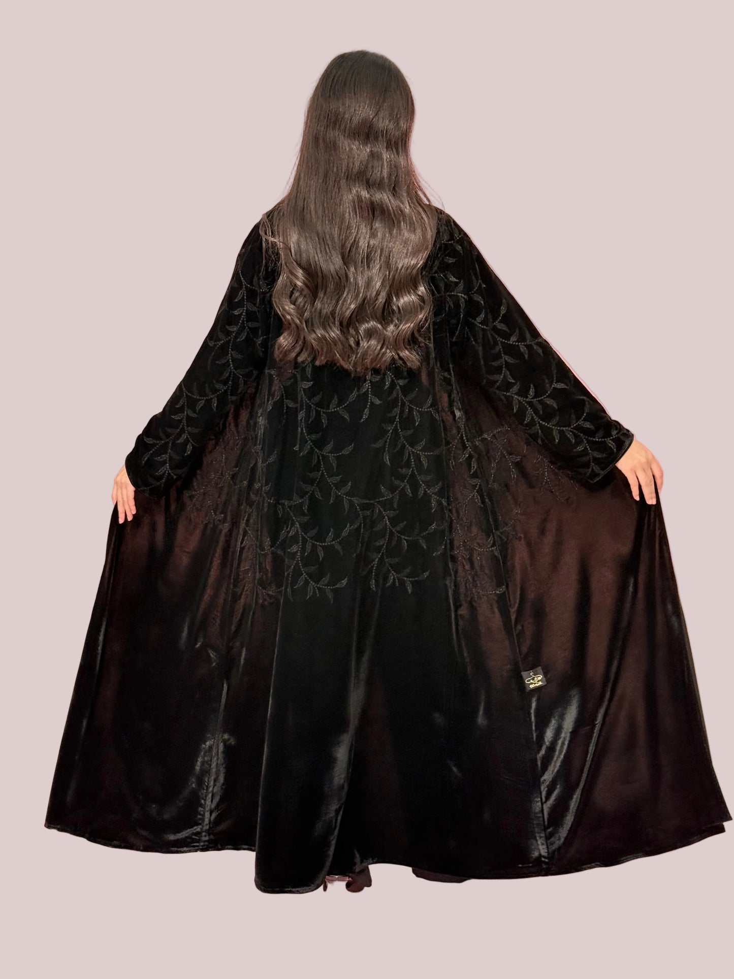 a woman wearing Premium Black Velvet Abaya with Tone-on-Tone Vine floral Embroidery on a pink background