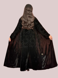 a woman wearing Premium Black Velvet Abaya with Tone-on-Tone Vine floral Embroidery on a pink background