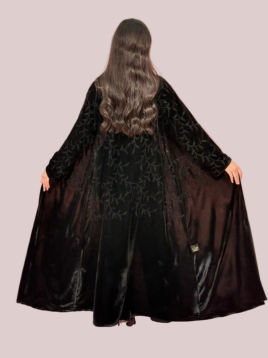 a woman wearing Premium Black Velvet Abaya with Tone-on-Tone Vine floral Embroidery on a pink background
