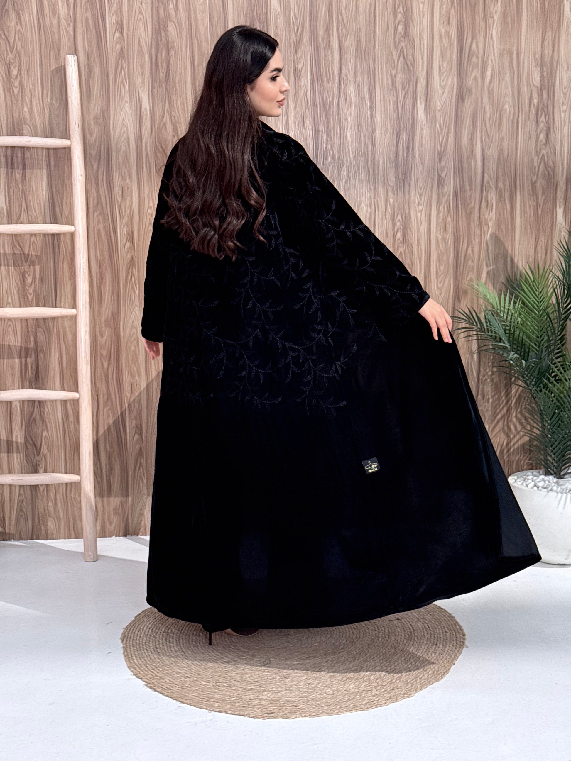 a woman wearing Premium Black Velvet Abaya with Tone-on-Tone Vine floral Embroidery on a pink background