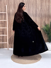 a woman wearing Premium Black Velvet Abaya with Tone-on-Tone Vine floral Embroidery on a pink background