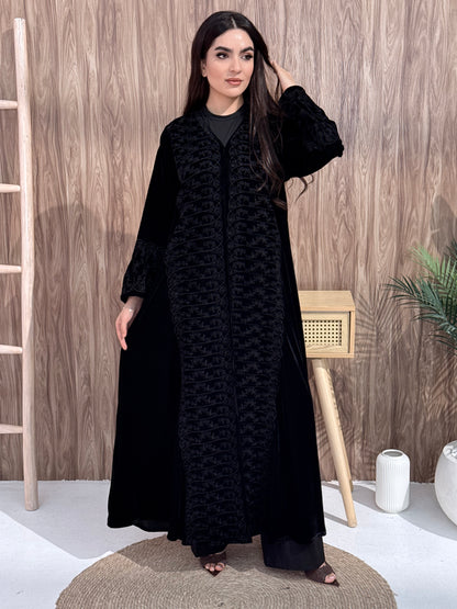 Woman wearing a black dress with a geometric pattern on a wooden floor.