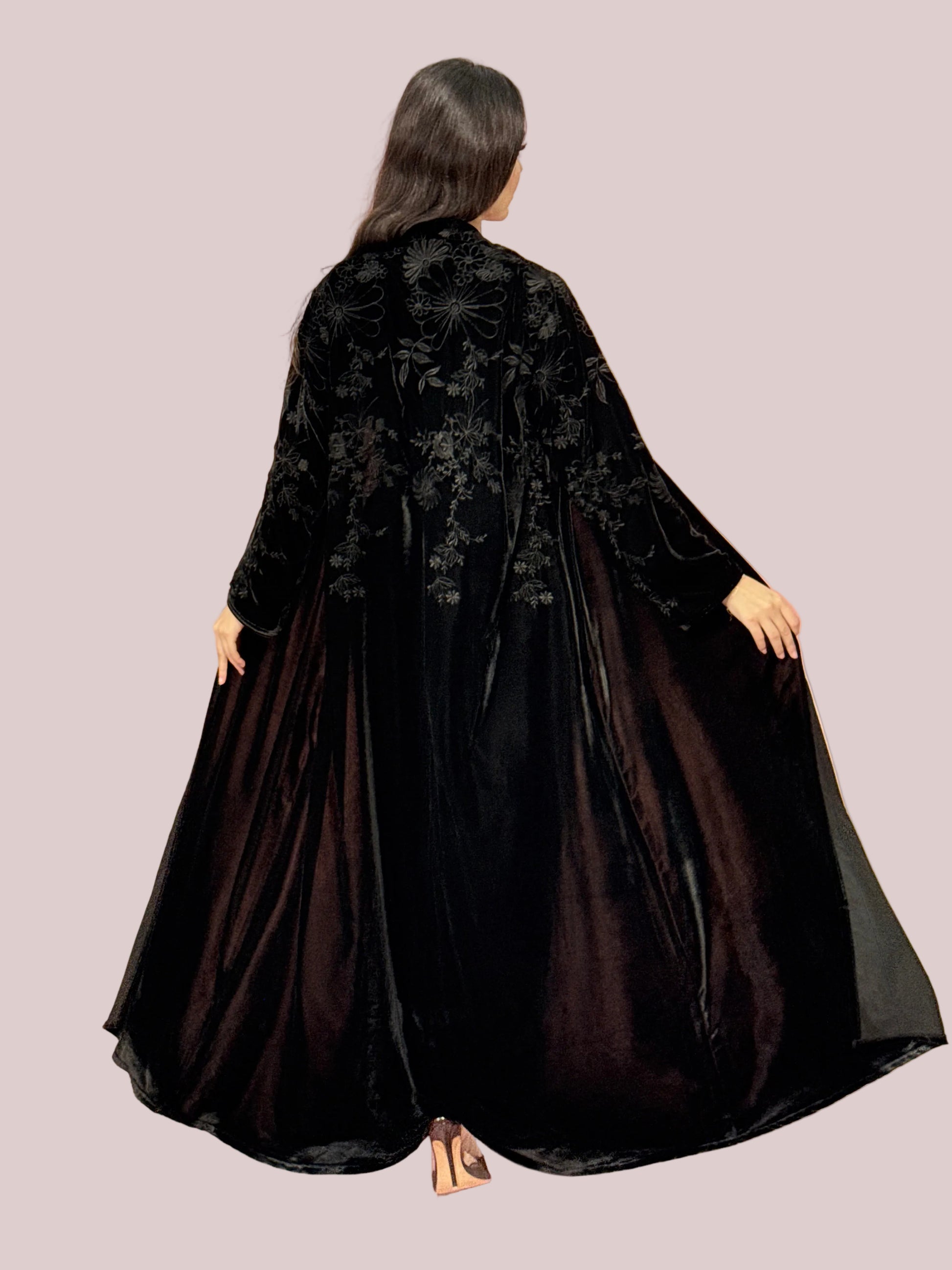 a lady wearing Premium Black Velvet Abaya with Floral Embroideryon a pink background