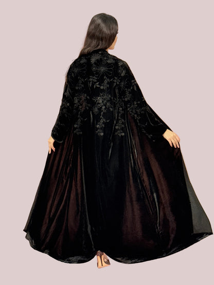 a lady wearing Premium Black Velvet Abaya with Floral Embroideryon a pink background