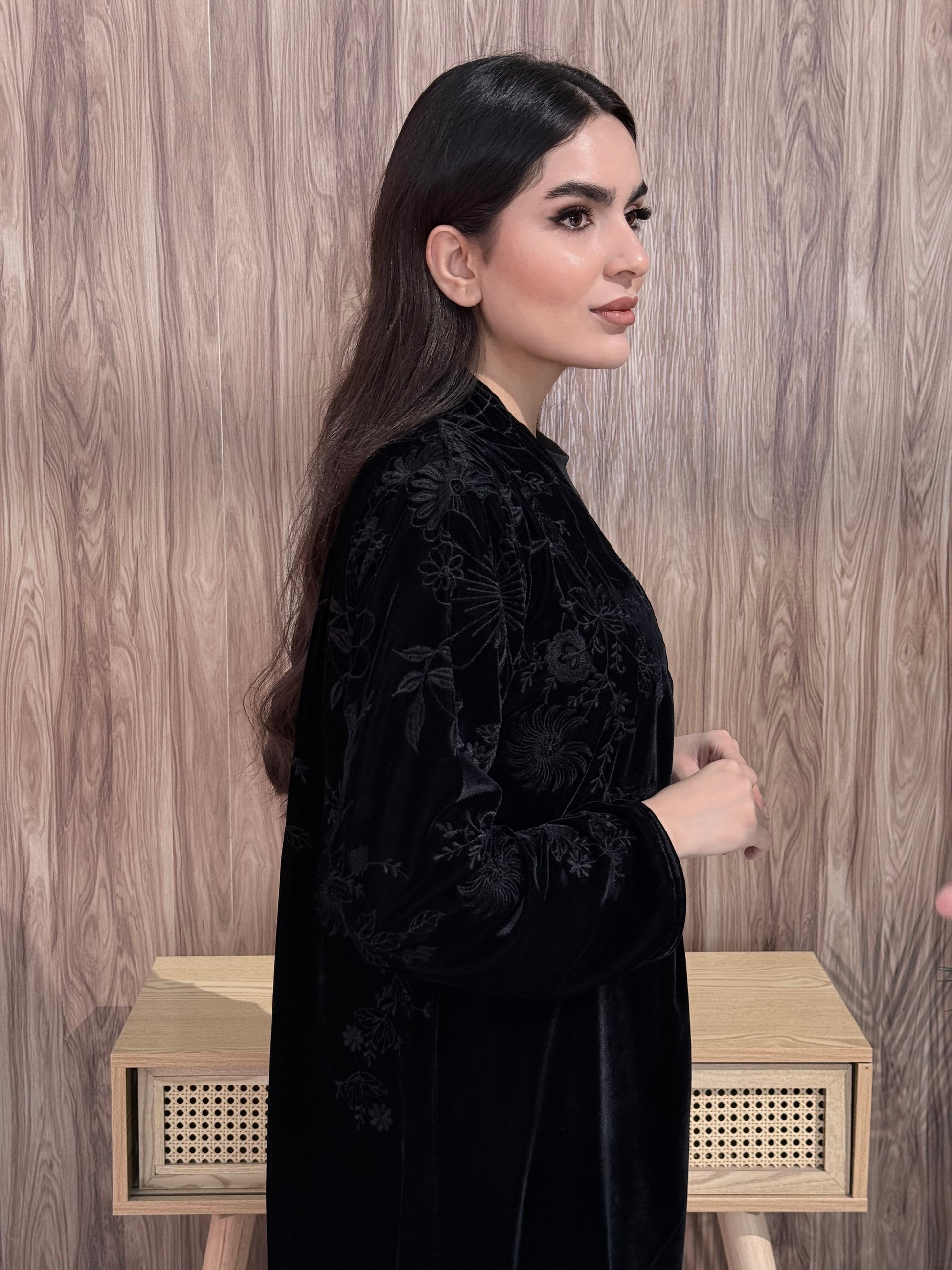Woman wearing a Premium Black Velvet Abaya with Floral Embroidery on a wooden floor.