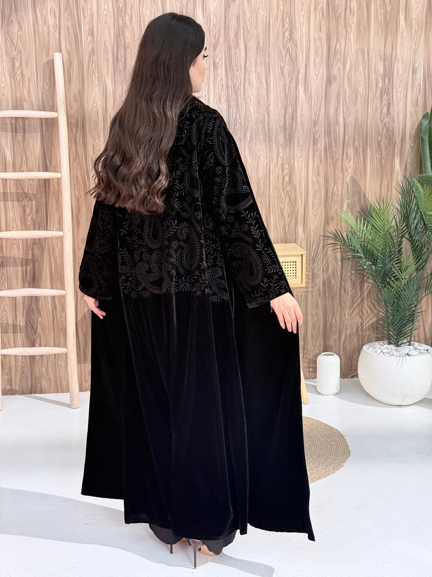 A person wearing a premium black velvet abaya coat with lace details in an indoor setting