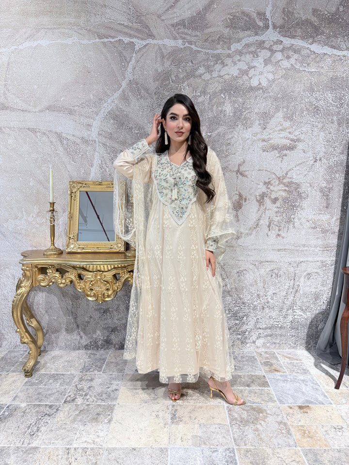 A woman in a long, Cream Luxury French Lace Tulle evening jalabiya Dress standing in a room with a decorative mirror.