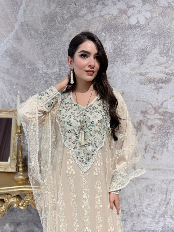 A woman in a long, Cream Luxury French Lace Tulle evening jalabiya Dress standing in a room with a decorative mirror.