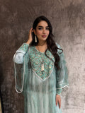 Woman in a light blue traditional outfit with floral patterns on a textured brown background