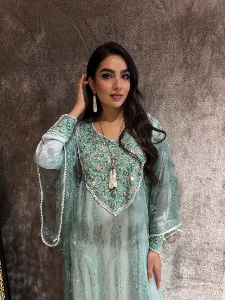 Woman in a light blue traditional outfit with floral patterns on a textured brown background