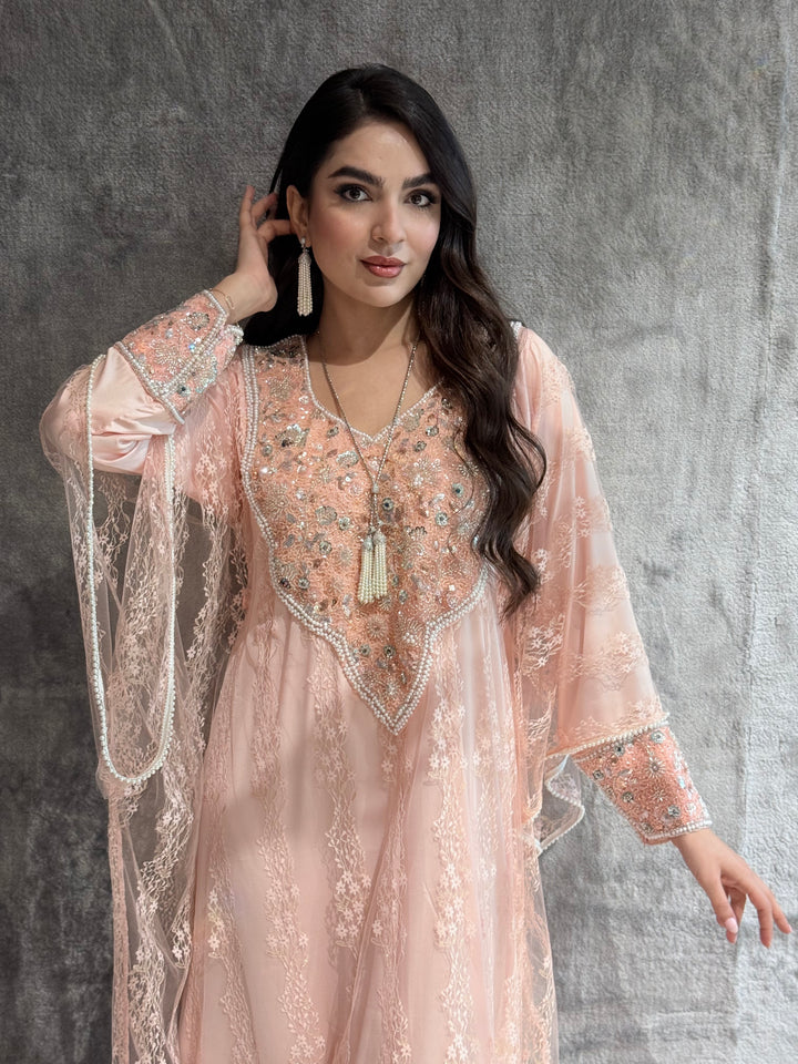 Woman wearing a light pink embroidered outfit against a gray background
