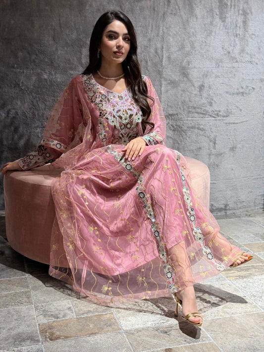 Woman in Dusty Pink Embroidered Tulle Thobe Dress against a gray stone wall.