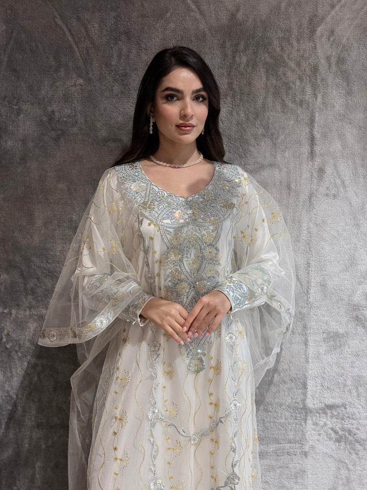 Woman wearing an Off White Embroidered  Authentic Emirati Thobe-inspired Design jalabiya against a gray textured wall.