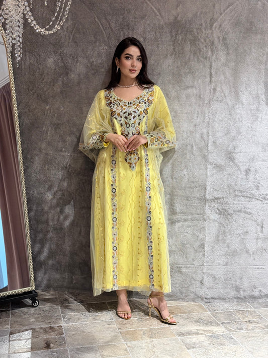 Woman wearing an yellow Embroidered  Authentic Emirati Thobe-inspired Design jalabiya against a gray textured wall.