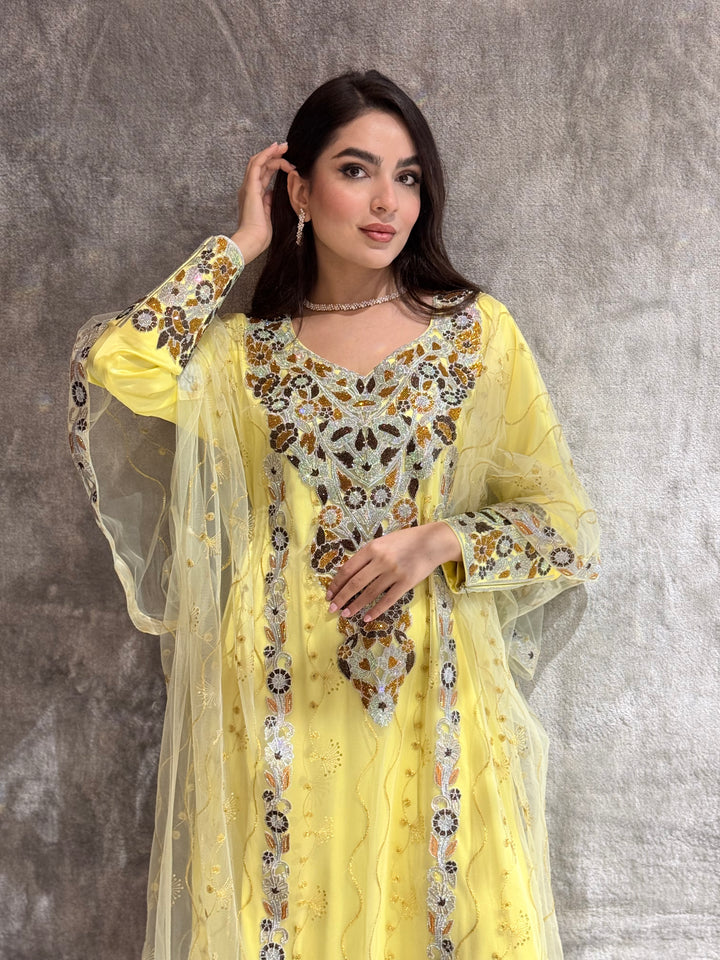 Woman wearing an yellow Embroidered  Authentic Emirati Thobe-inspired Design jalabiya against a gray textured wall.