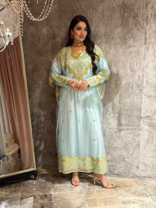 Woman wearing a light blue embroidered jalabiya with gold details against a brown background