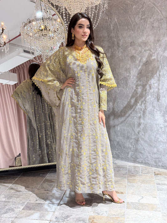 Woman in a long,  Grey Luxury Embroidered Kaftan Dress standing in a room with decorative elements.