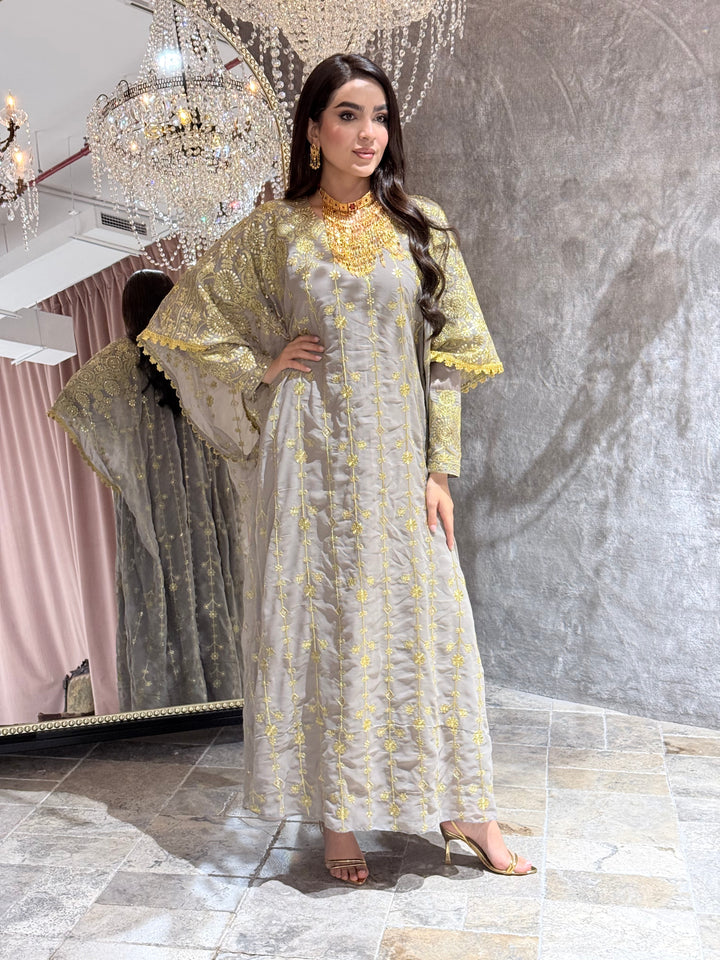 Woman in a long,  Grey Luxury Embroidered Kaftan Dress standing in a room with decorative elements.