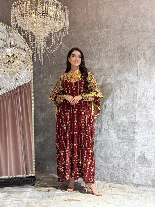 Woman wearing a maroon and gold embroidered kaftan outfit on a textured gray background