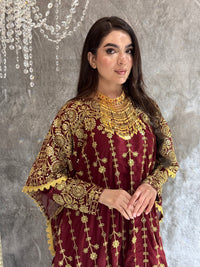 Woman wearing a maroon and gold embroidered kaftan outfit on a textured gray background