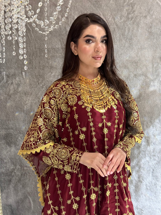 Woman wearing a maroon and gold embroidered kaftan outfit on a textured gray background