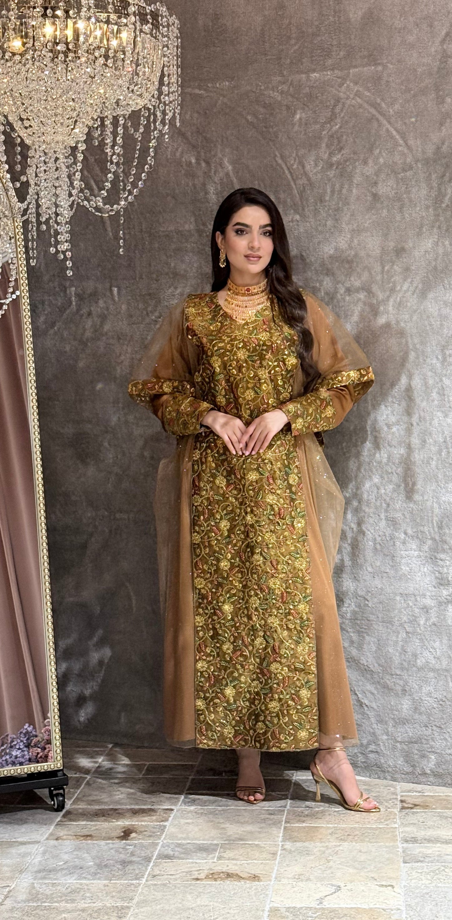 Woman in a Golden Brown Floral Embroidered Kaftan standing on a reflective floor with a chandelier in the background