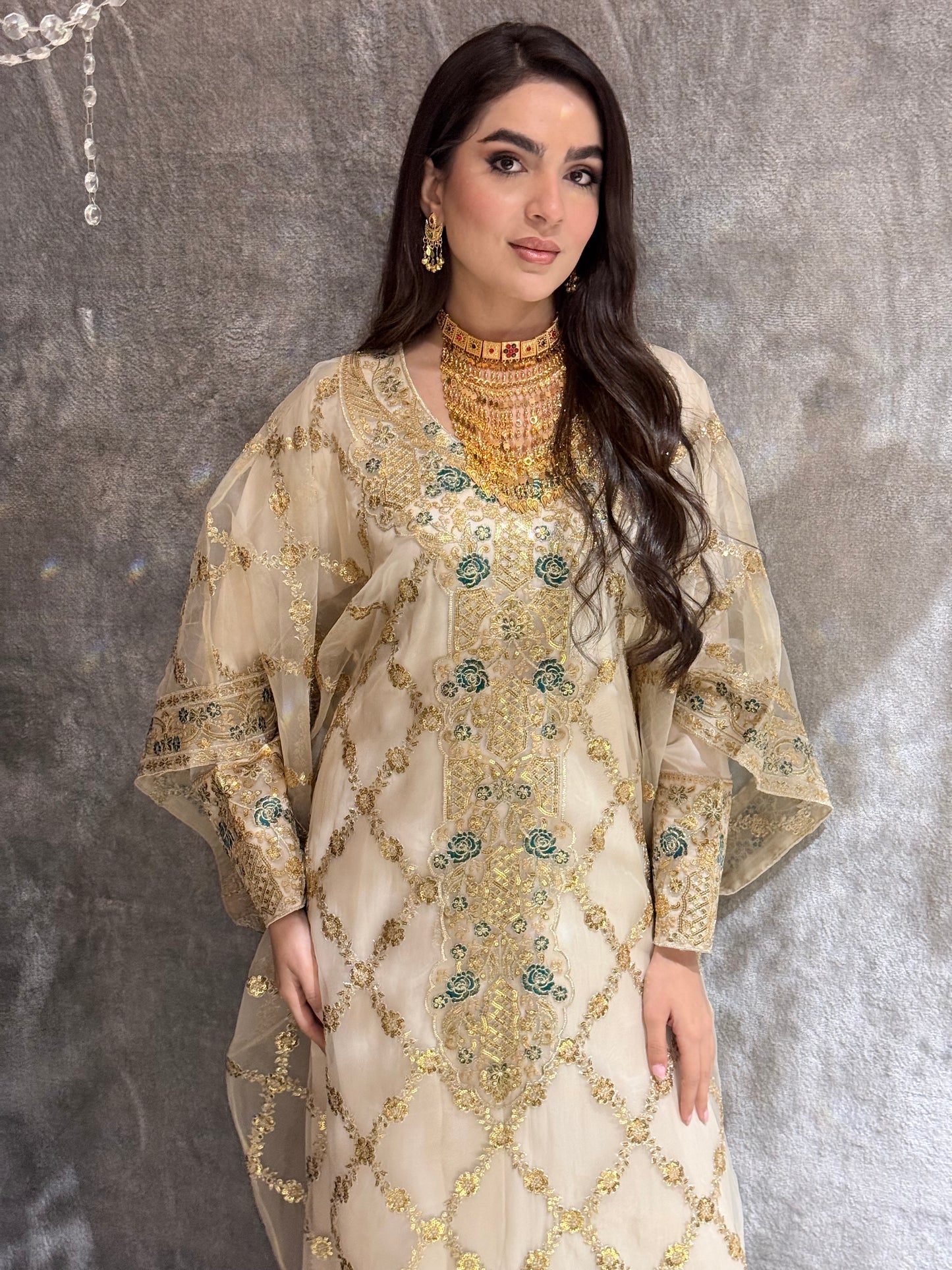 Woman wearing a traditional Beige Luxury Embroidered Kaftan outfit on a textured gray background