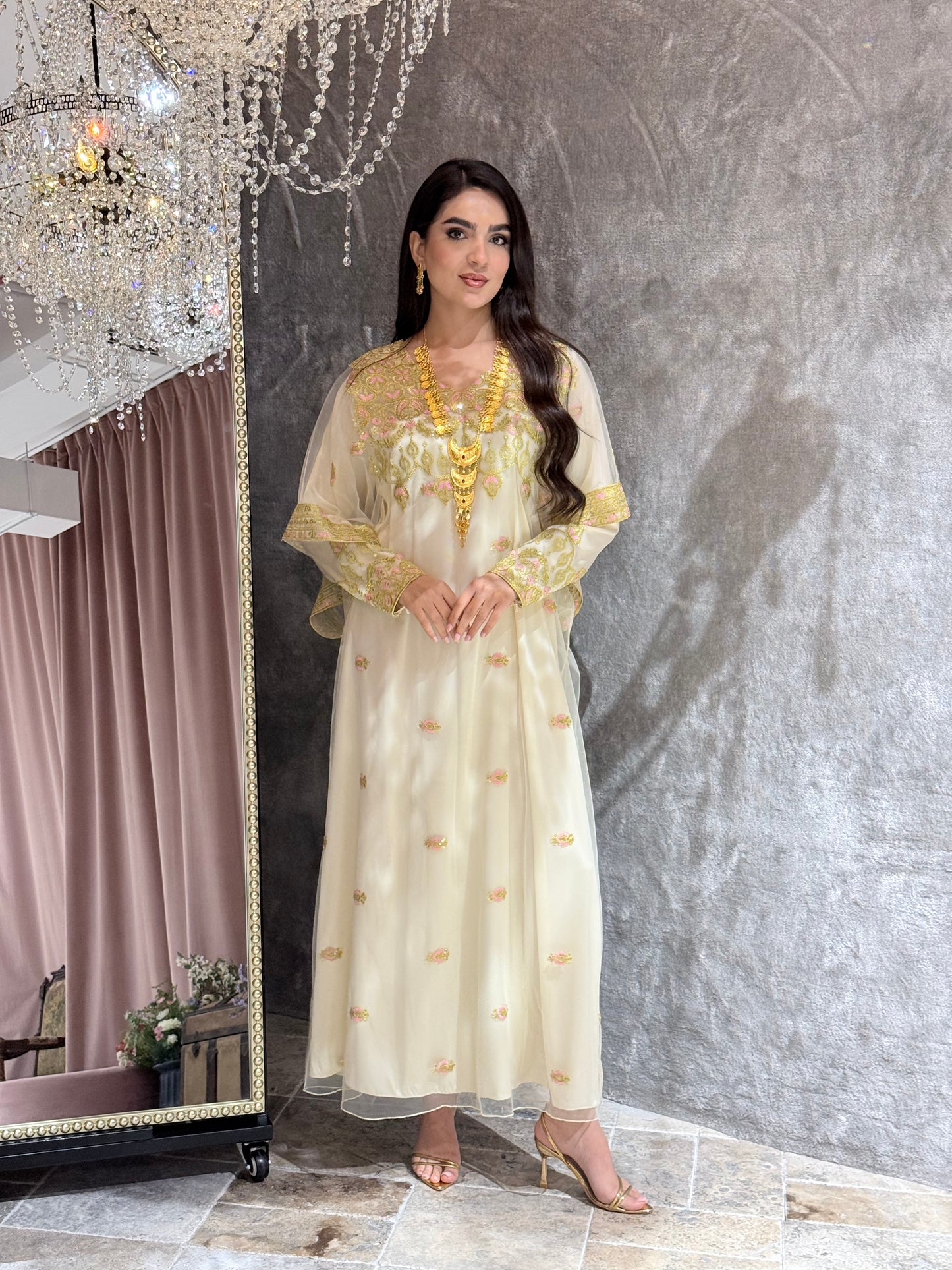 Woman in a Cream Luxury Embroidered Kaftan dress with gold accents standing in front of a mirror.