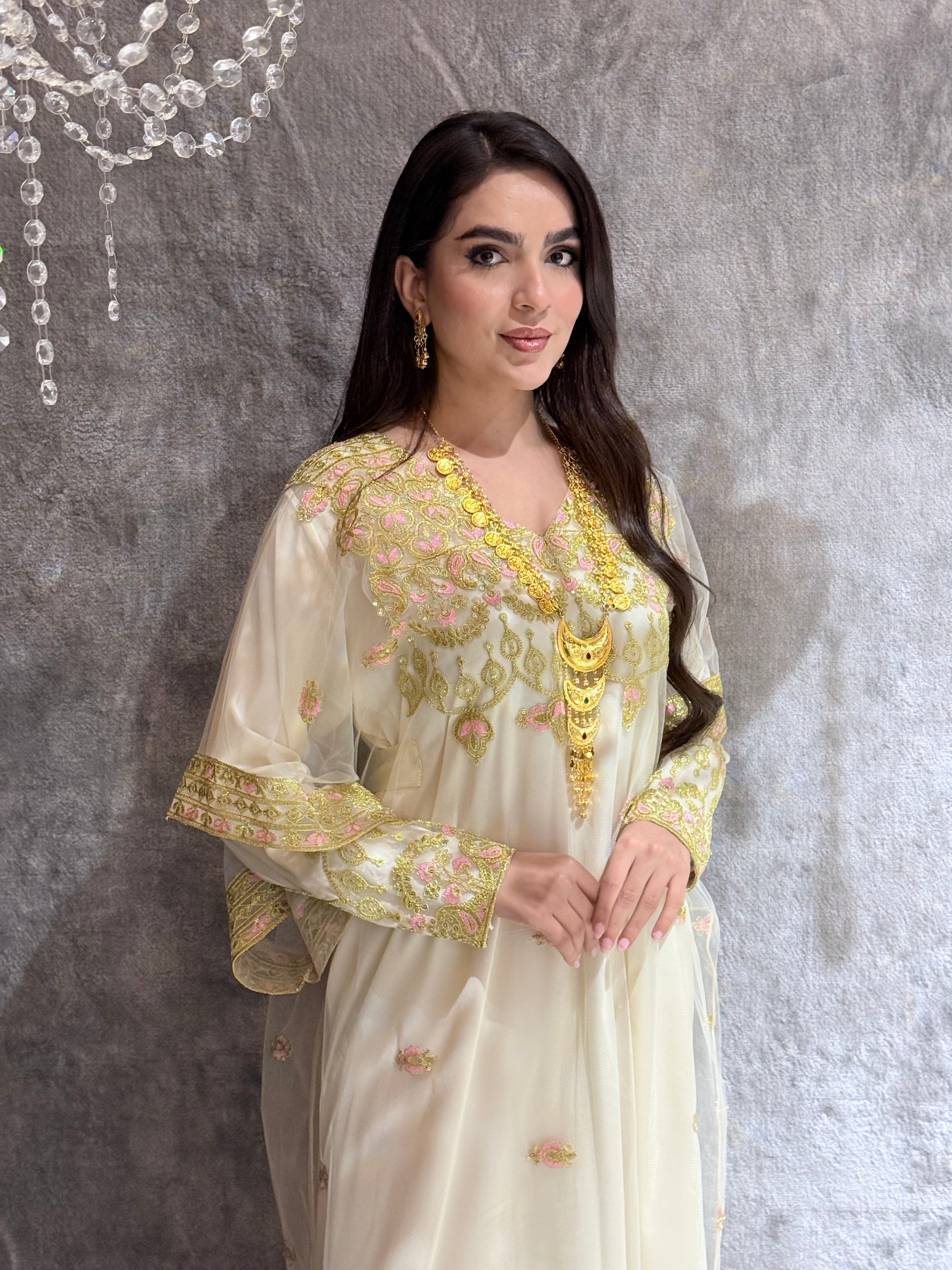 Woman in a Cream Luxury Embroidered Kaftan dress with gold accents standing in front of a mirror.