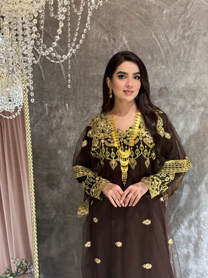 Woman wearing a dark brown traditional kaftan outfit with gold embroidery on a textured gray background